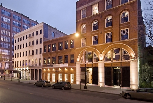 Street view of 220-230 West Kinzie St., Chicago, showcasing historic brick buildings with arched windows and illuminated architectural details.