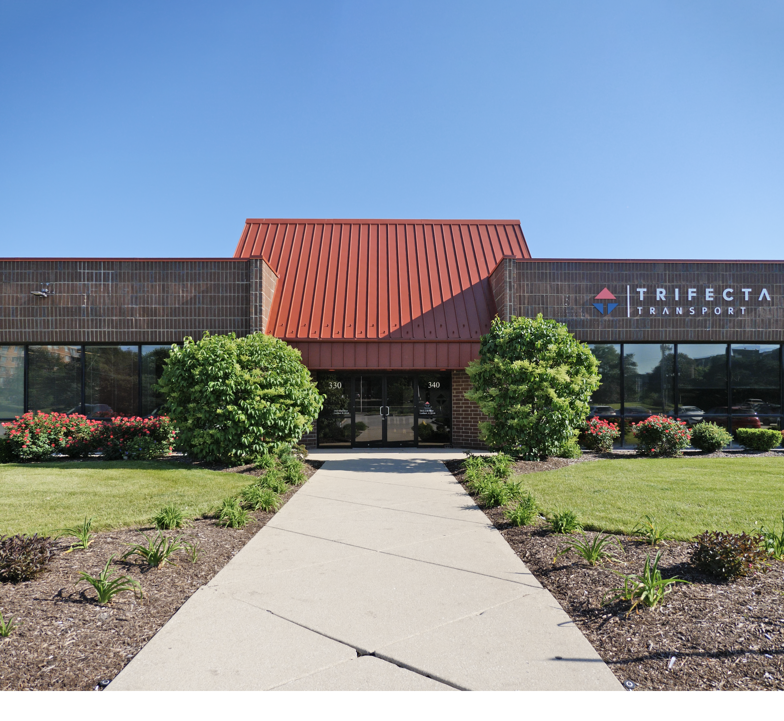 Street view of 350 E. 22nd St., Lombard, IL 60148, showcasing a commercial building with a red metal roof and brick facade surrounded by landscaped greenery.